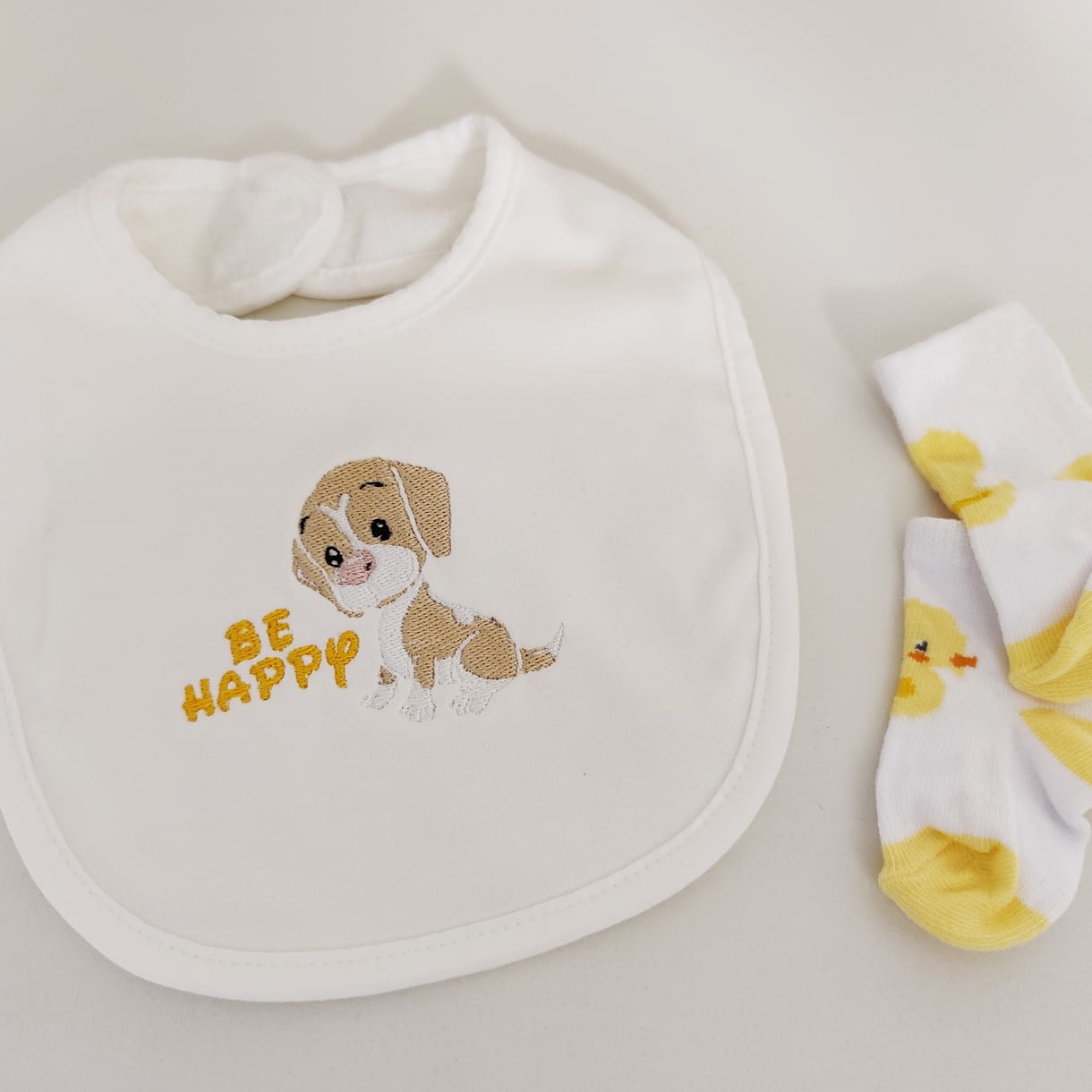 Fotografia bavaglino cagnolino con scritta Be Happy e calzini per bambini