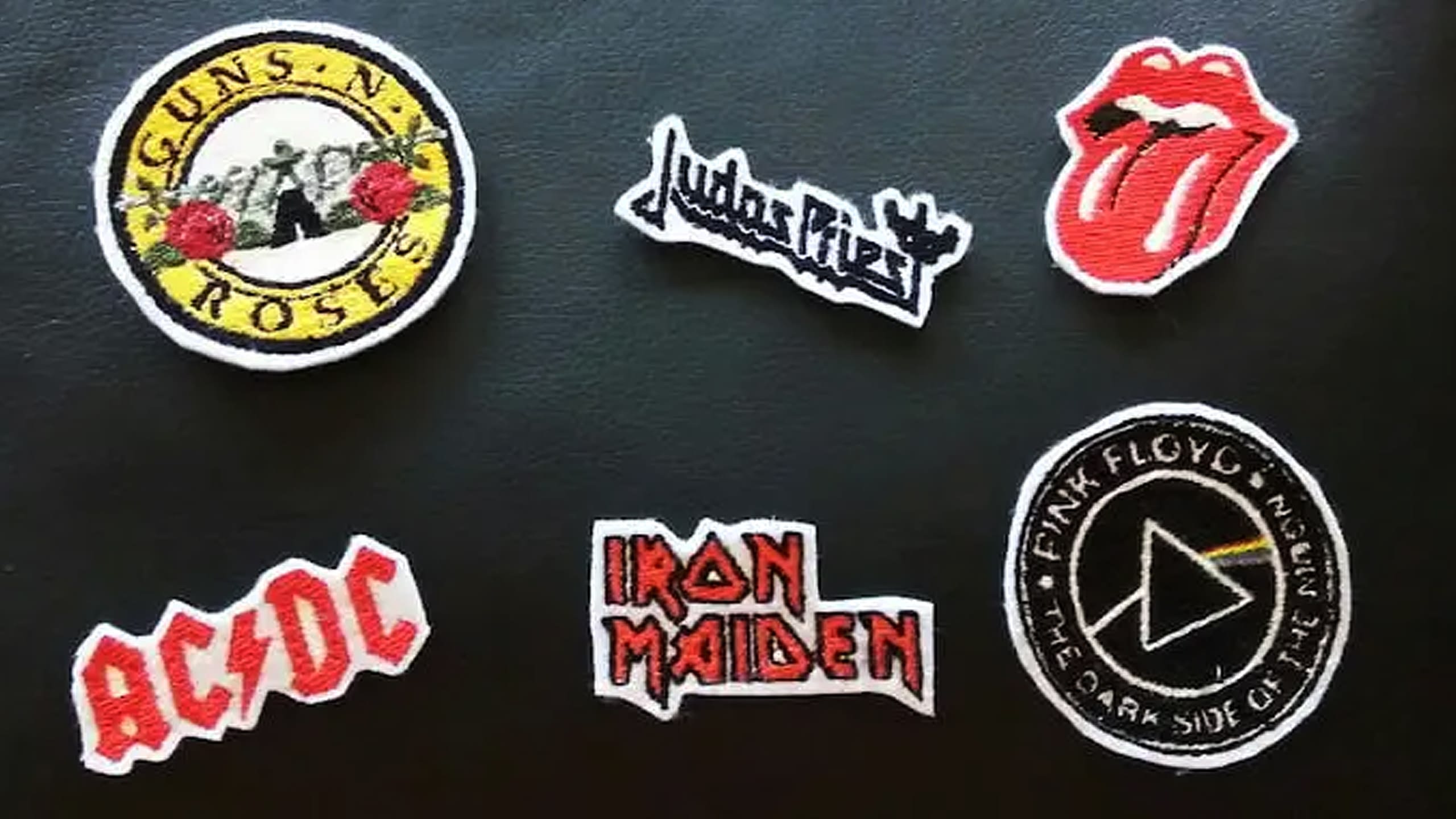 Fotografia di una pochette in pelle nera con i loghi ricamati delle band Guns n'Roses, Judas Priest, Rolling Stones, AC/DC, Iron Maiden e Pink Floyd